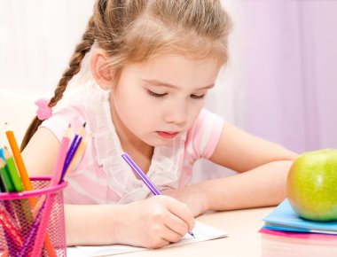 Cute little girl is writing at the desk clipart