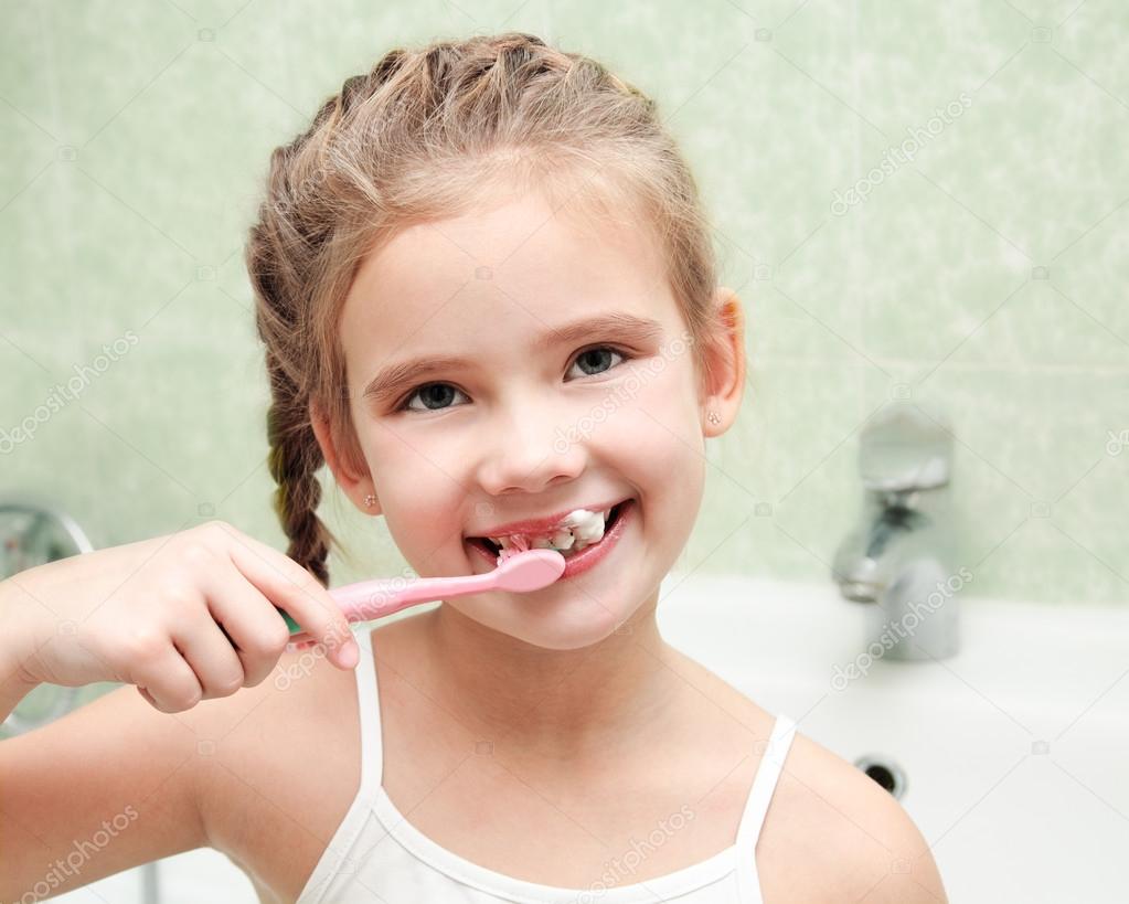 Smiling cute little girl brushing teeth in bathroom