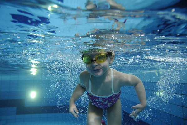 Divertente felice bambino ragazza nuotare sott'acqua in una piscina con un sacco di bolle d'aria — Foto Stock