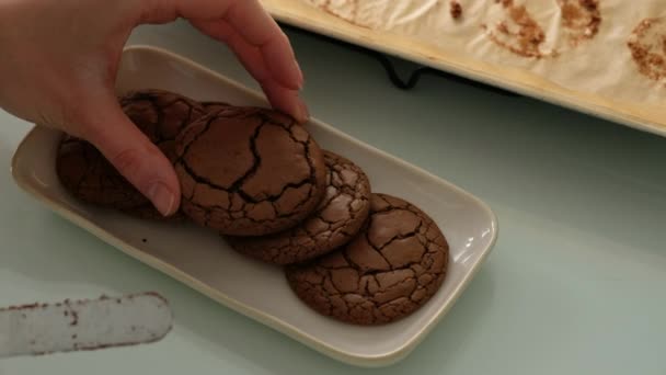 Čerstvě uvařené čokoládové sušenky. Ženské ruce rozkládají čokoládové sušenky z pečiva na talíři na skleněném stole. Detailní záběr. — Stock video