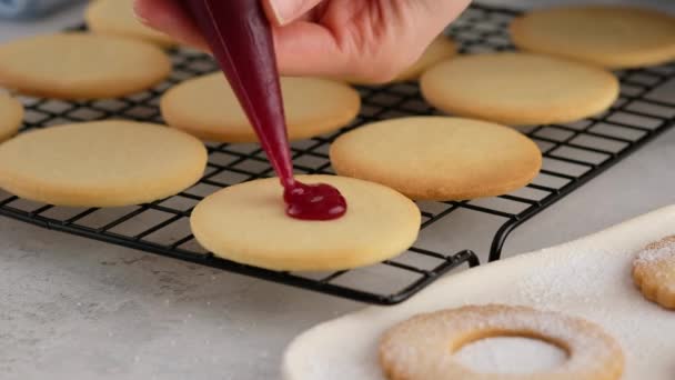 Жінки кладуть варення на печиво з кондитерського пакету. Жіночі руки виготовляють домашнє печиво з пісочного печива з джемом. Курабське печиво з малиновим джемом. Різдвяне печиво з джемом . — стокове відео