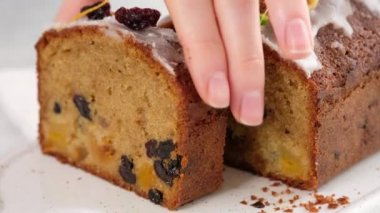 Kadın eli bir parça kek alır ve yerine koyar. Arka planda fenerler olan bir Noel atmosferi. Ev yapımı Noel çöreği. Kurutulmuş meyveli kek. Geleneksel kek Noel için..