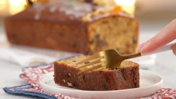 La mano femenina rompe un trozo de un bifurcador en rodajas de pastel de frutas. Ambiente navideño con linternas al fondo. Pastelito casero de Navidad. Panecillo tradicional con frutas secas para Navidad. — Vídeos de Stock