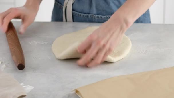 Gros plan des mains des femmes étaler la pâte avec un rouleau à pâtisserie en bois sur une table lumineuse pour faire du pain de blé. Nous préparons du pain blanc dans une boulangerie professionnelle à partir de farine, eau, huile, sel. — Video