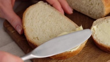 Ağır çekim. Kadın elinin tereyağını mutfak bıçağıyla odun bir masanın üzerinde dilimlenmiş buğday ekmeğine sürmesi. Beyaz ekmek profesyonel bir pastanede hazırlanır..