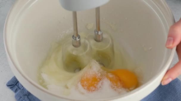 Mixing egg whites, yolks and sugar in a ceramic bowl with a hand mixer on a white table. Cooking a sponge cake. — Stock Video