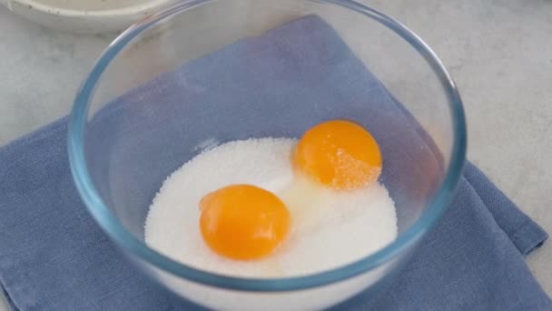 Close-up van de vrouwelijke handen zetten ingrediënten in een kom voor het maken van room. Melk, suiker en eieren mengen in een kom op een witte tafel. Een biscuitje bakken met Charlotte Cream. — Stockvideo