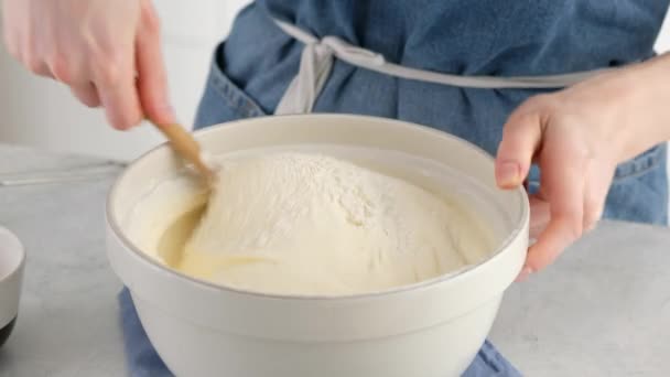 Vrouwelijke handen roeren bloem met losgeklopte eieren om een spons cake te maken. Mengen van ingrediënten in kom op een witte tafel. Een spons cake bakken. — Stockvideo