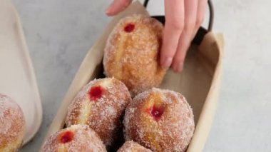 Yakın çekim kamera hareketi. Berlinliler. Kadın eli, beyaz arka planda servis tepsisine ahududu reçelli donut damlatan bir donut koyar. Lezzetli tatlı çörekler. Reçelli çörek yapıyorum..