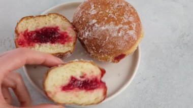 Berlinliler. Kadın eli, beyaz arka plandaki bir tabağa ahududu reçelli bir çörek koyar. Dolgulu kesilmiş bir çörek. Lezzetli tatlı çörek. Reçelli çörek yapıyorum..