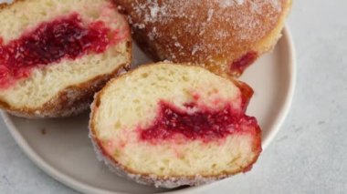 Yakın çekim kamera hareketi. Berlinliler. Ahududu reçelli çörekler beyaz arka planda bir tabakta duruyor, içi dolmuş kesilmiş bir donut. Lezzetli tatlı çörek. Reçelli çörek yapıyorum..