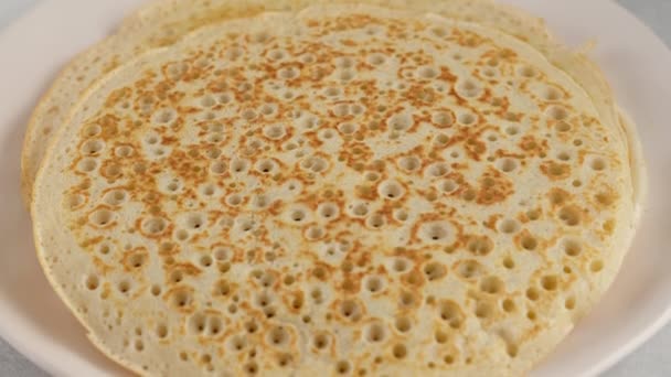 Leg de pannenkoek op een bord en vet in met boter. Grote ronde pannenkoek. Er komt rook uit pannenkoeken. Pannenkoeken met kefir. Pannenkoeken met gaten. Pannenkoekenweek. Russische traditie. — Stockvideo