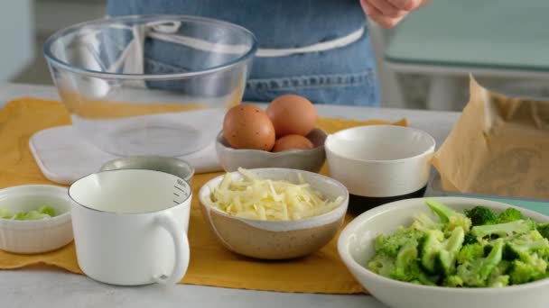 Ingredienserna ligger på bordet och ägget läggs i en glasskål för broccoli och ostpommes frites i en bakform. Italiensk frukost. Bakad hackad omelett med grönsaker. Sund frukost. — Stockvideo