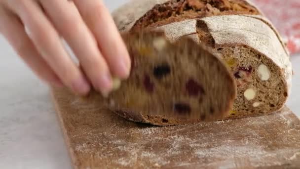 Красиві жіночі руки кладуть шматок сільського житнього хліба на дерев'яну дошку. Хліб з ячмінного солоду, борошна, солі та сухофруктів. Земгальський хліб з сухофруктами . — стокове відео
