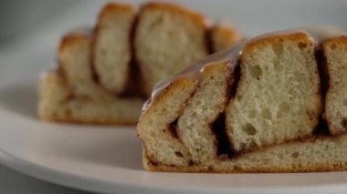 Tarçınlı rulo ekmeği bir tabakta yakın plan kesim. Tarçınlı ruloların üzerine tatlı krem peynirli krema dökülüyor. Tarçınlı çörek üretimi. Fırın ürünleri. Aperatif tarçınlı çörekler