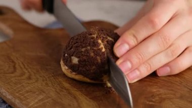 Choux ya da profiterol pişirirken, kadın tahta tahtada choux kesiyor, yakın plan. Çikolatalı craquelin ile kremalı ve çilekli choux pişiriyorum. Vanilyalı choux çikolatalı craquelin..