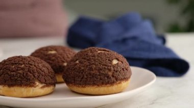 Choux ya da profiterol pişirme, kadın elleri choux üzerine şeker serpiştirme, yakın çekim. Çikolatalı craquelin ile kremalı ve çilekli choux pişiriyorum. Vanilyalı choux çikolatalı craquelin..