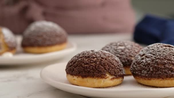 Cocinar choux o profiteroles, manos femeninas espolvorear azúcar glaseado en choux, primer plano. Cocinar cremoso y choux de bayas con craquelina de chocolate. Choux de vainilla con craquelina de chocolate. — Vídeos de Stock