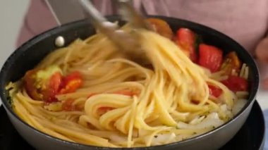 Bir tava pastası. Kadın bir aşçının yakın plan resmi. Bir tava makarna pişiriyor ve içine karıştırıyor..