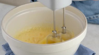 Seramik bir kasede yumurta beyazı, yumurta sarısı ve şekeri beyaz bir masada el çırpıcı ile karıştırıyorum. Sünger keki pişiriyorum..