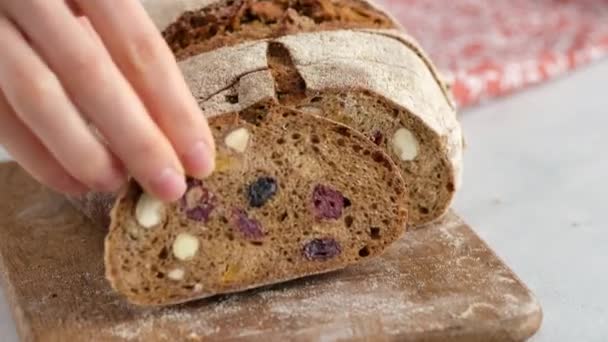 Beautiful female hands put a piece of rustic rye bread on a wooden board. Bread made from barley malt, flour, salt and dried fruit. Zemgale bread with dried fruits. — Videoclip de stoc