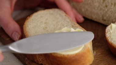 Ağır çekim. Kadın elinin tereyağını mutfak bıçağıyla odun bir masanın üzerinde dilimlenmiş buğday ekmeğine sürmesi. Beyaz ekmek profesyonel bir pastanede hazırlanır..