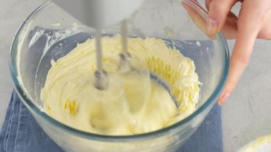 Beyaz bir masada elektrikli mikserle krema yapmak için cam bir kâsede tereyağı çırpılan kadın ellerine yakın plan. Charlotte kremalı pandispanya pişiriyorum..