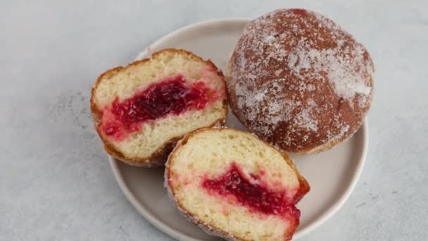 Close-up camera movement. Berliners. Donuts with raspberry jam lie on a plate on a white background, a cutaway donut with a filling flowing out. Delicious sweet donut. Making donuts with jam. — Stock Video