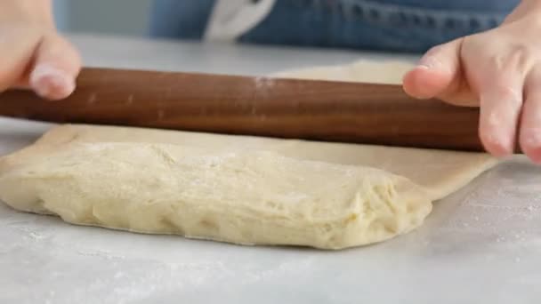 De belles mains féminines roulent la pâte avec un rouleau à pâtisserie en bois dans une cuisine professionnelle et préparent la pâte pour la fabrication du pain et des petits pains. Du pain à la levure. Pain à base de lait, beurre, farine, œufs et levure. — Video