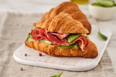 Taze kruvasan ya da salatalıklı sandviç, jambonlu jambonlu, prosciutto, ahşap arka planda. Sabah kahvaltısı kavramı. Sağlıklı ve fast food.