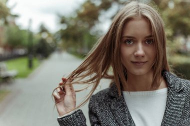 Güzel, sarışın, genç bir manken. Gri, kalın bir palto giymiş. Şehir Bulvarı 'nda kameraya poz veriyor.