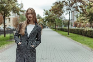 Gri yün ceketli güzel bir kadın ara sokakta dikiliyor ve kameraya bakıyor.