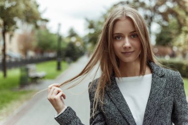 Güzel, sarışın, genç bir manken. Gri, kalın bir palto giymiş. Şehir Bulvarı 'nda kameraya poz veriyor.