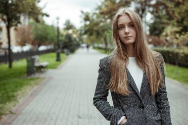 Gri yün ceketli güzel bir kadın ara sokakta dikiliyor ve kameraya bakıyor.