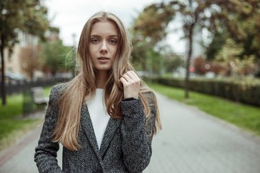 Gri yün ceketli güzel bir kadın ara sokakta dikiliyor ve kameraya bakıyor.