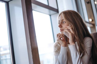 Güzel bir kadın cep telefonundan arıyor ve pencereden bakıyor.