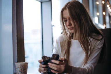 Kadın fotoğrafçı kafede oturuyor ve fotoğraf makinesi kullanıyor.