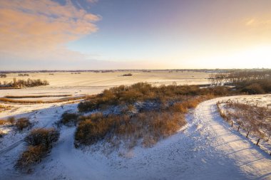 Kış mevsiminde mavi gökyüzünün altında tepeler ve çayırlar olan karlı bir manzara. Alım Parkı Hayvanat Bahçesi, Hollanda