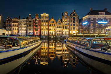 Amsterdam Damrak geleneksel Hollanda mimarisi geceleri. Ön planda tur tekneleri.