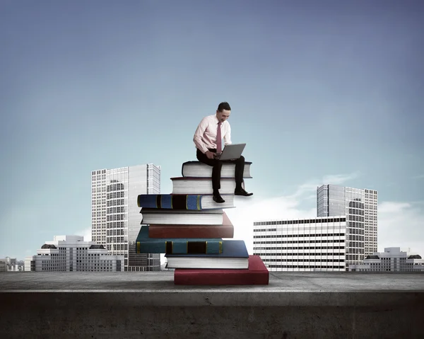 Бизнесмен, работающий с ноутбуком на вершине книг — стоковое фото