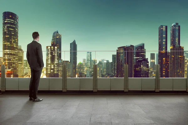 Businessman standing on a roof and looking at city — Stock Photo, Image