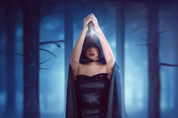 Femme sorcière avec manteau noir a couteau tenu haut et est prêt à poignarder — Photo