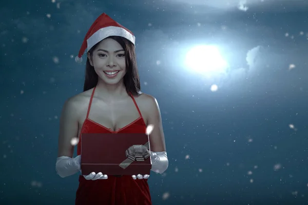 身穿圣诞老人服装的亚洲女人在降雪时拿着礼品盒 背景是夜景 圣诞快乐 — 图库照片