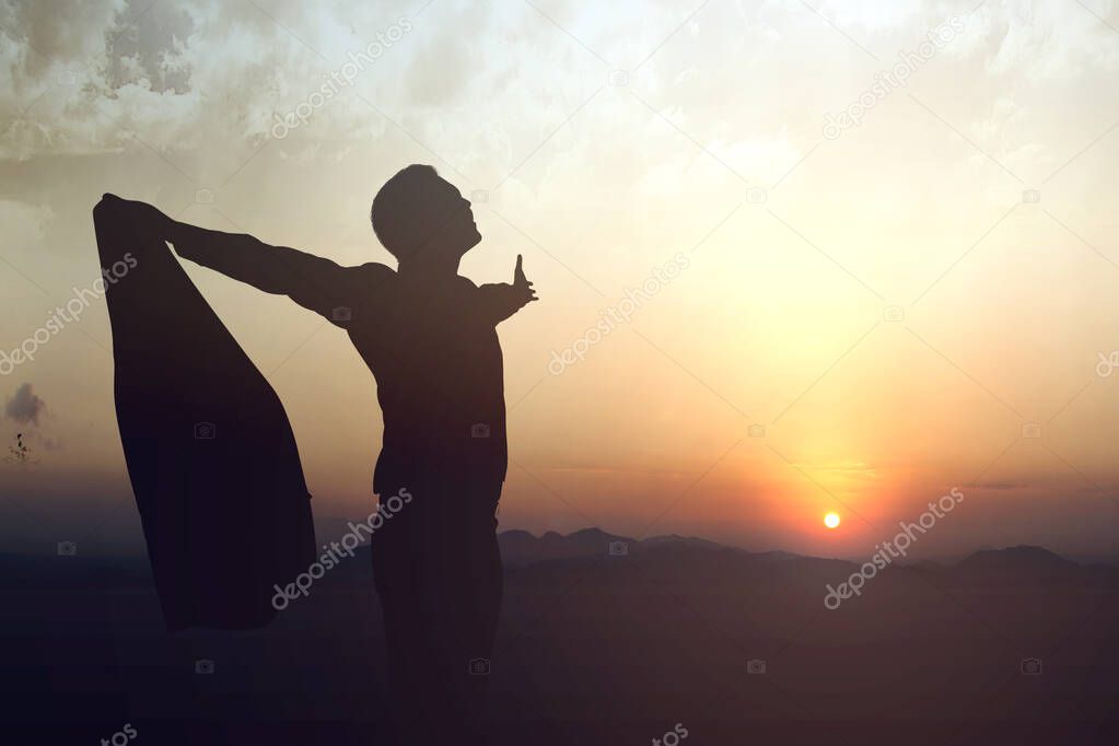 Silhouette of businessman raised hands and praying to god with a sunset sky background