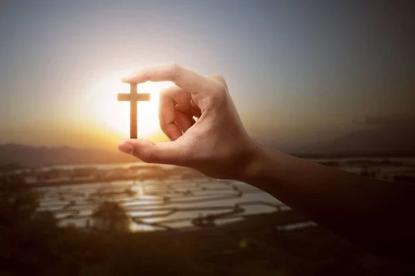 人的手牵着有日落背景的基督教十字架 — 图库照片