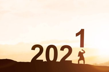 İş adamının silueti 2021 'i tepenin tepesine, günbatımının arka planına yerleştirdi. Mutlu yıllar 2021