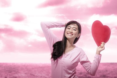 Kırmızı kalbi dramatik bir gökyüzü arka planıyla tutan Asyalı kadın. Sevgililer Günü