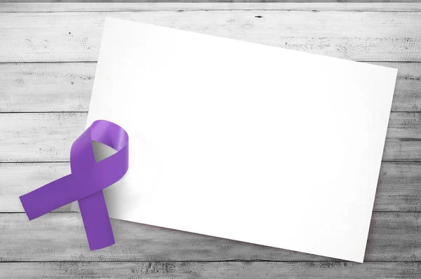 Purple ribbons with blank white paper on wooden background. World Cancer Day concept. Blank white paper for copy space