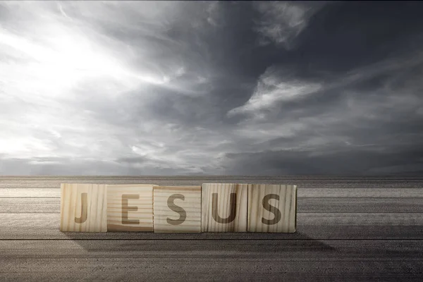 Wooden cube with Jesus text on wooden table with a dramatic sky background