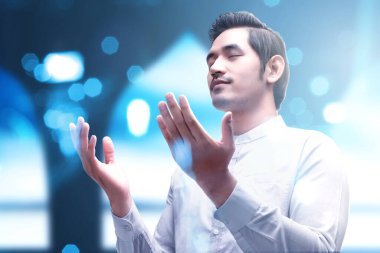 Asyalı Müslüman adam elini kaldırdı ve arka planı bulanık bir şekilde dua etti.